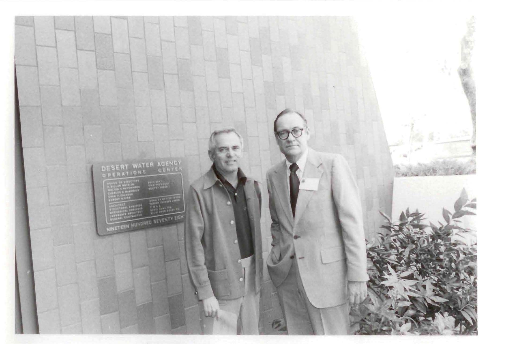Two men pose in front of the Desert Water Agency Operations Center, captured in a black-and-white photograph.