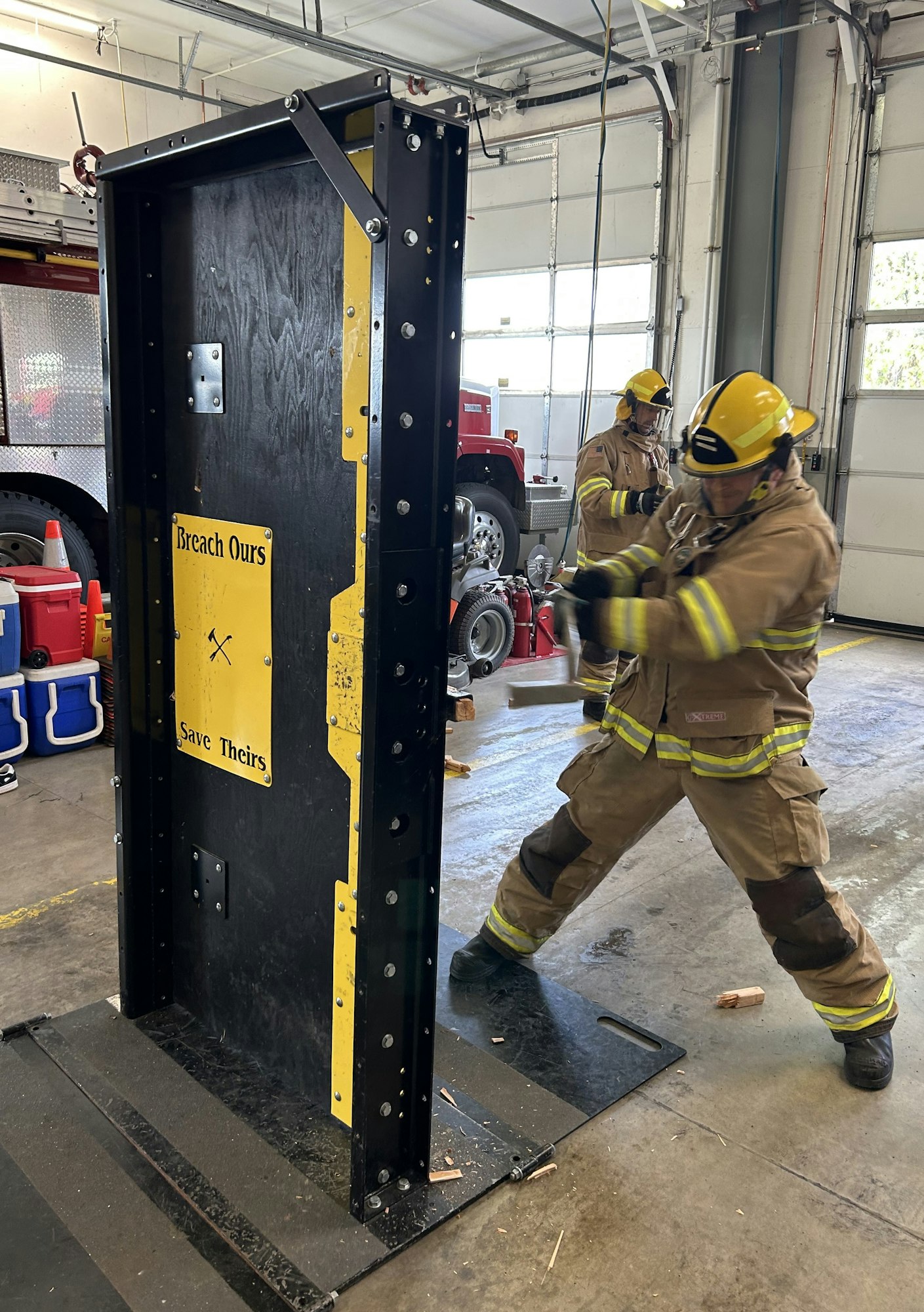 Firefighters are training to breach a door, emphasizing teamwork and safety with a focus on saving lives.
