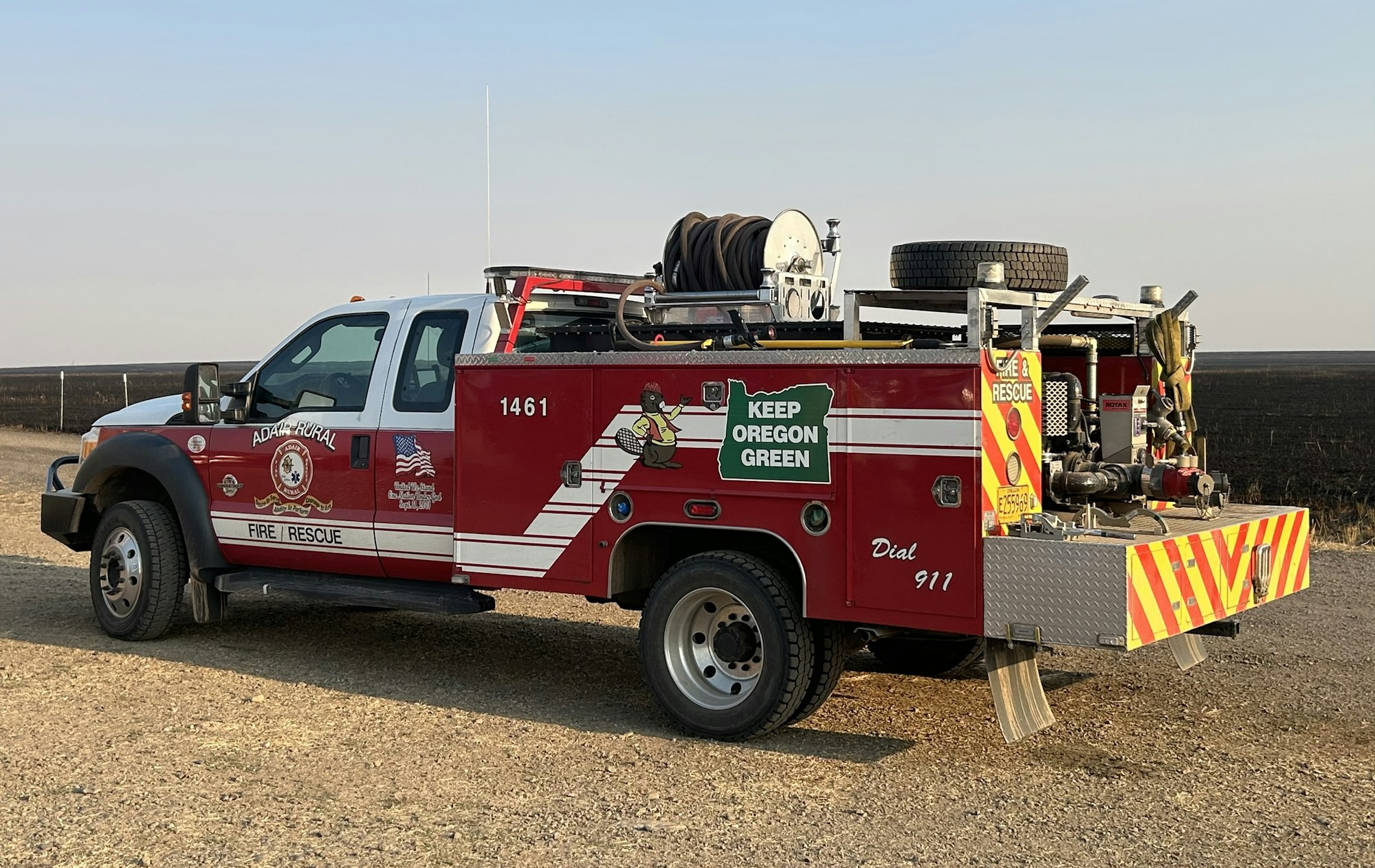 A red fire rescue truck with equipment, standing on a road with a clear sky in the background.