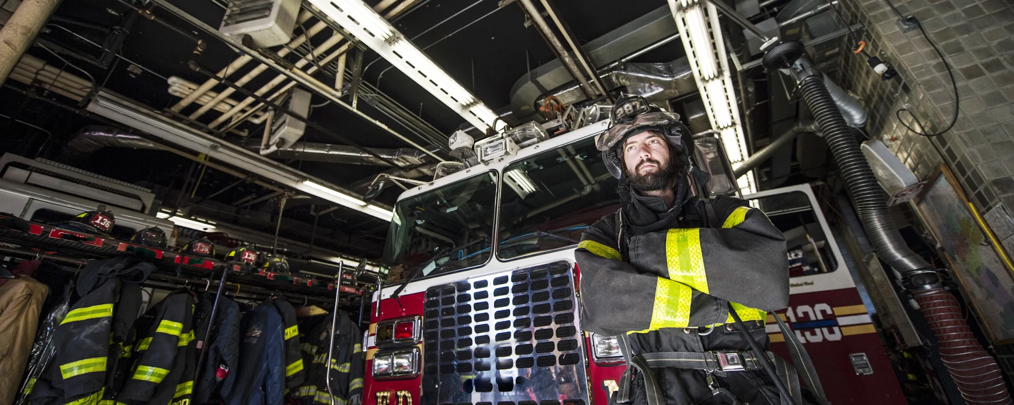 A firefighter in gear in front of a firetruck inside a fire station.