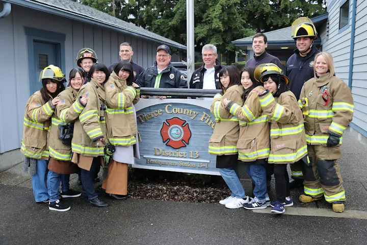 A group of firefighters and individuals in firefighting gear pose together at Pierce County Fire District 13 headquarters.