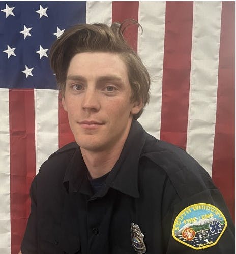 A person in a firefighter uniform in front of an American flag.