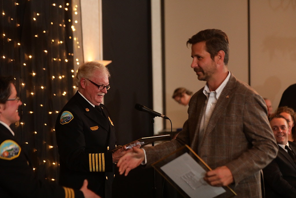 May contain: person, human, tie, accessories, accessory, suit, clothing, coat, overcoat, apparel, microphone, electrical device, crowd, and audience