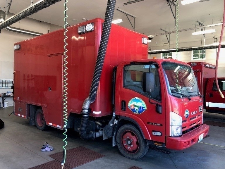 Red service truck in a garage, likely a firefighting support vehicle, with exhaust extraction system attached.