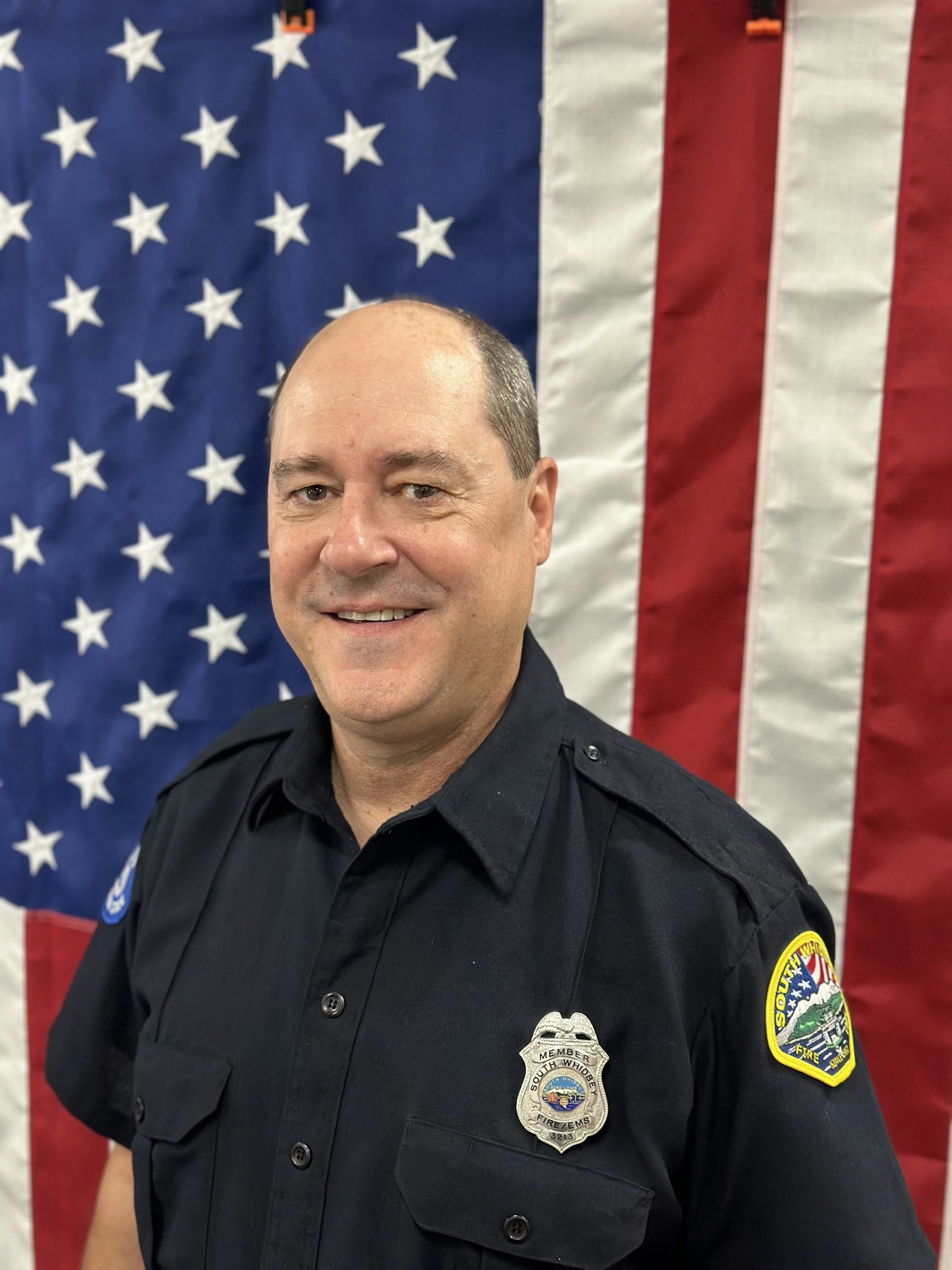 A man in a uniform with a badge, in front of an American flag.