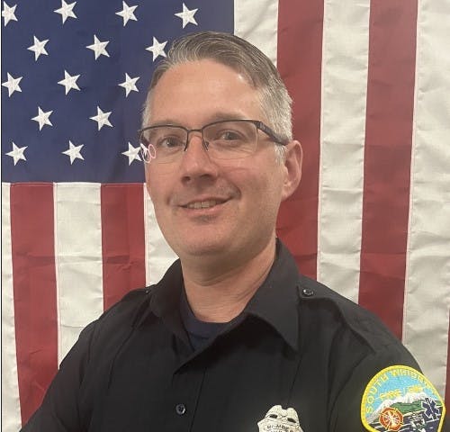 A person in a police uniform in front of an American flag.