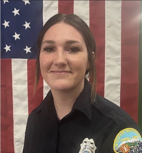 A woman in a uniform with a badge in front of an American flag.