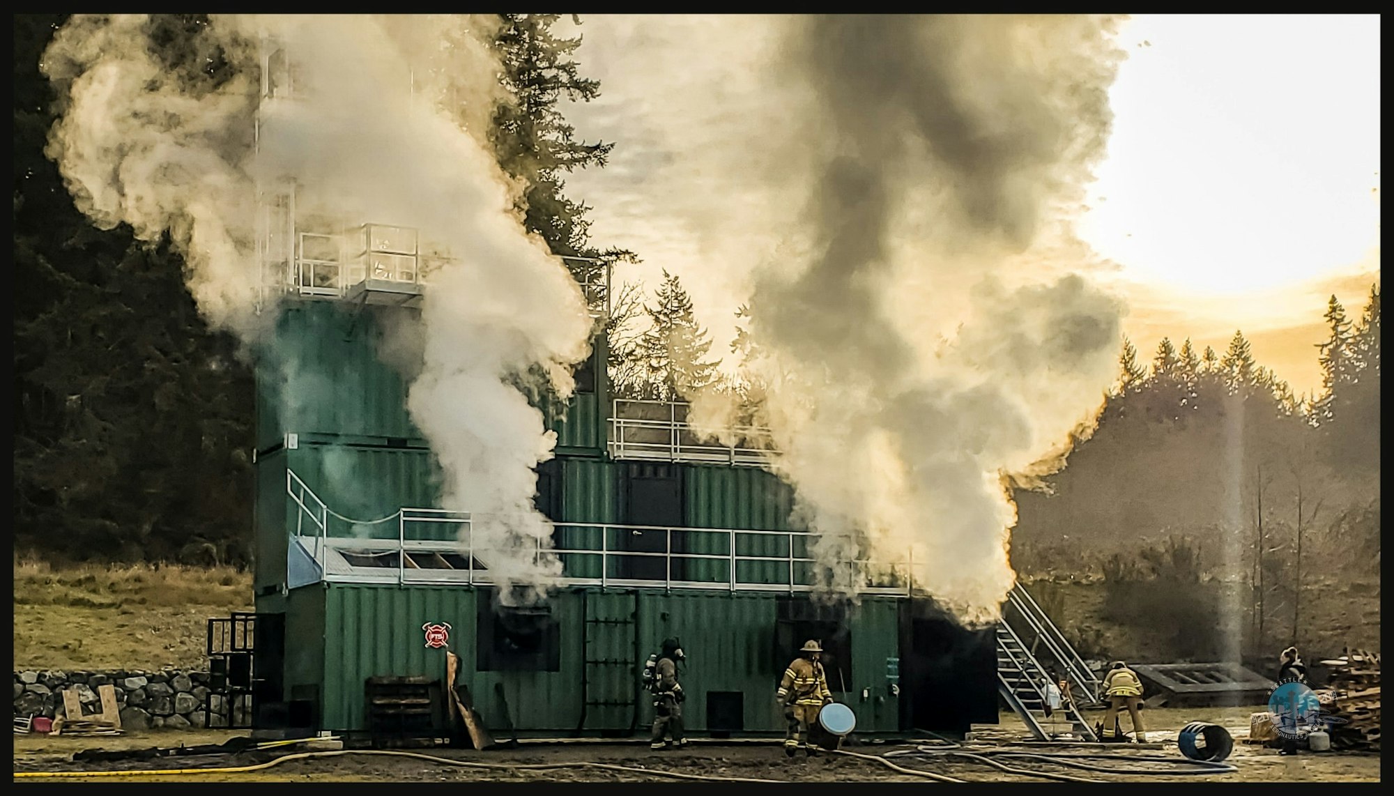 Firefighters training at a smoke-filled facility, responding to a controlled burn scenario in a forested area.