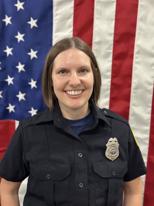 A person in a uniform with a badge in front of an American flag.