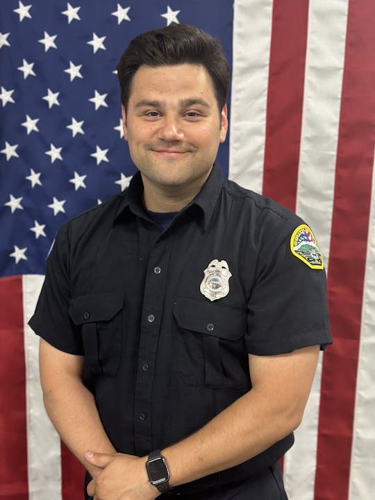A person in a uniform with a badge in front of the American flag.