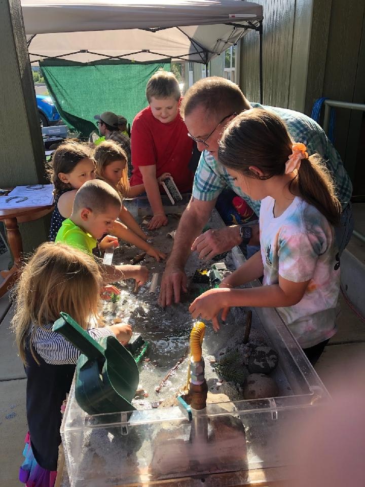 Children and an adult engaging in a water play activity outdoors under a canopy.