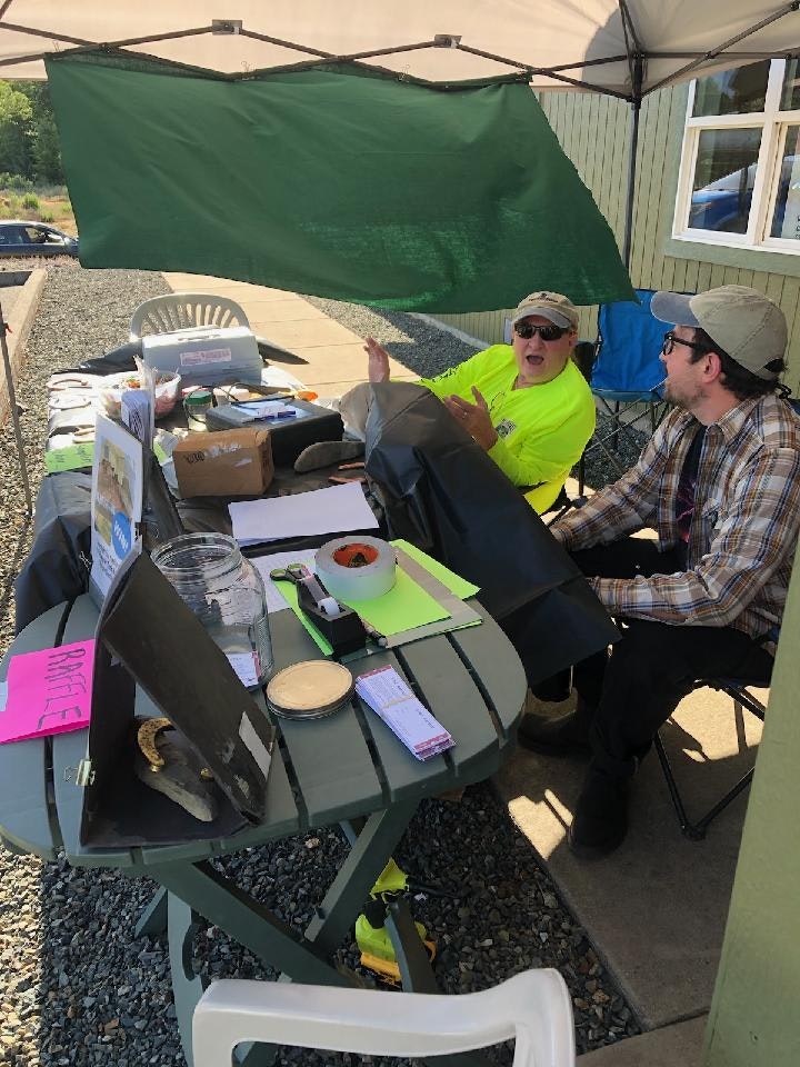Two people at a makeshift outdoor station with papers and a green canopy.