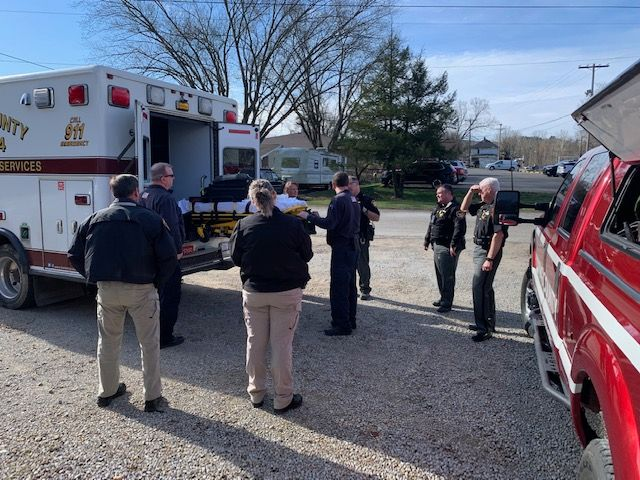 A group of emergency responders stands by an ambulance and red SUV in a parking area.