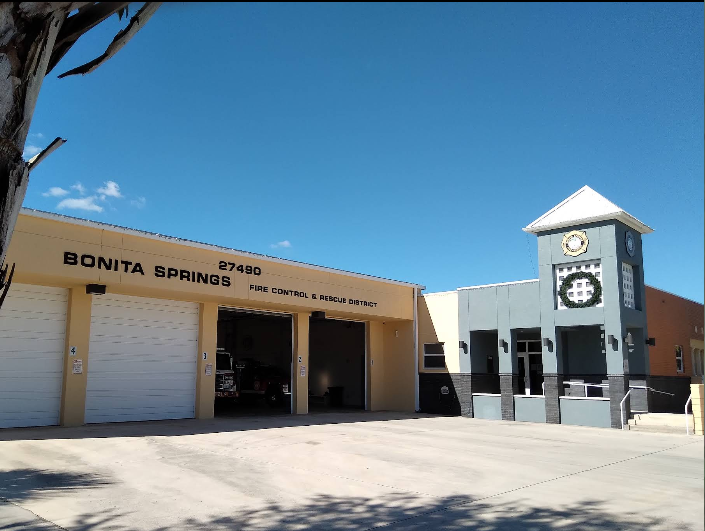 Image shows Bonita Springs Fire Control & Rescue District with garage doors and a clock tower building in clear blue sky.