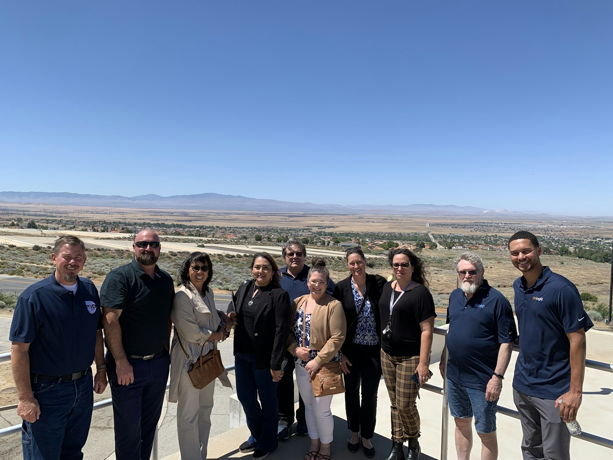A group of people poses together outdoors with a scenic view of a valley and mountains in the background.