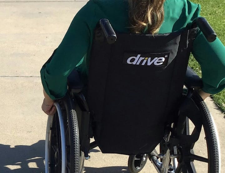 A person in a green shirt is in a "Drive" wheelchair on a sidewalk.
