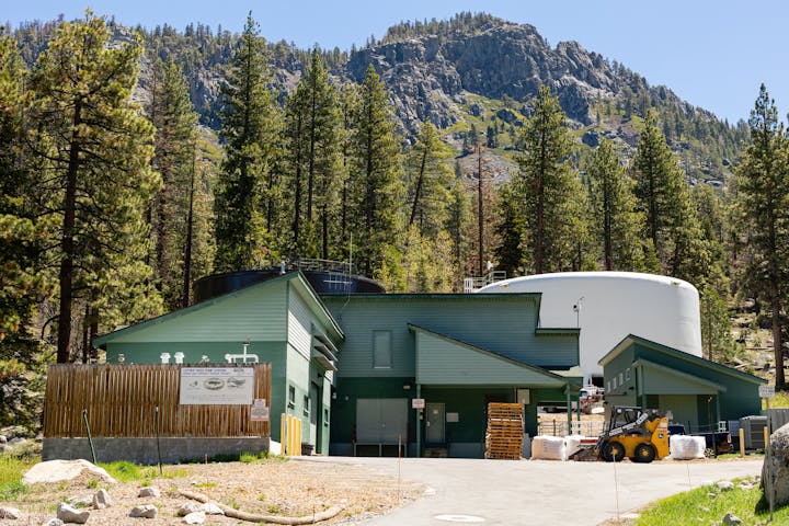 Luther Pass Pump Station with tanks and forklift surrounded by pine trees and a rocky hill in the background.