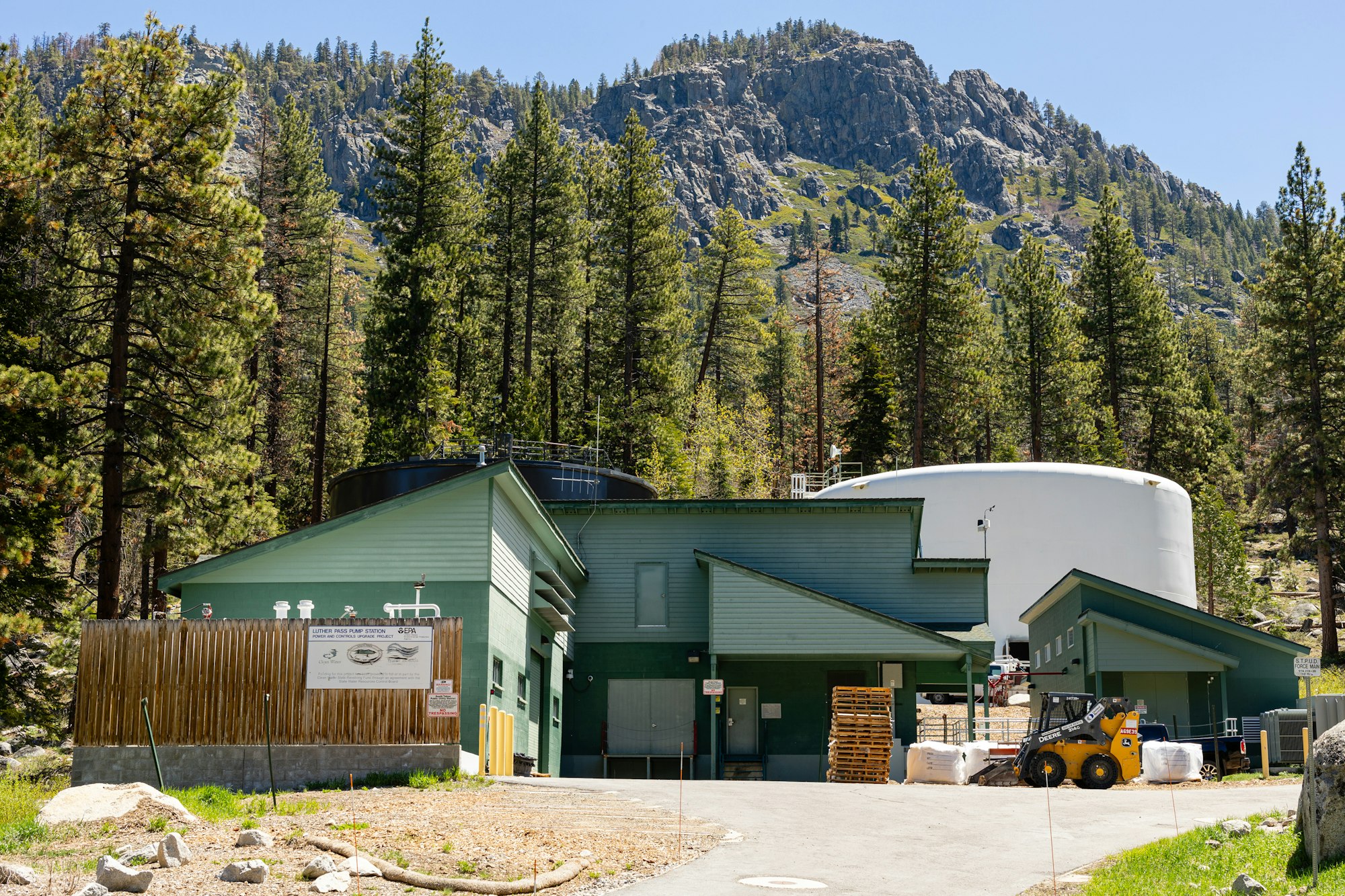 Luther Pass Pump Station with tanks and forklift surrounded by pine trees and a rocky hill in the background.