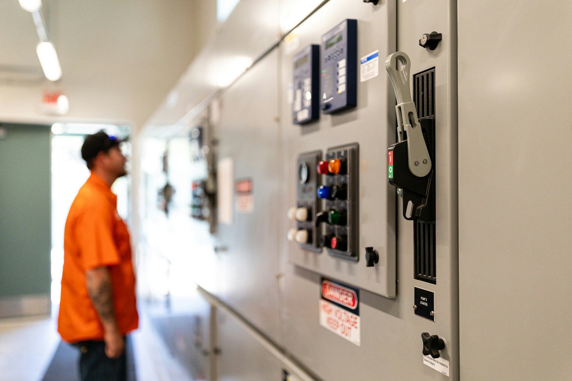 Luther Pass Pump Station control panel with various switches and a pumps crew working in an orange shirt looking at it, slightly out of focus.