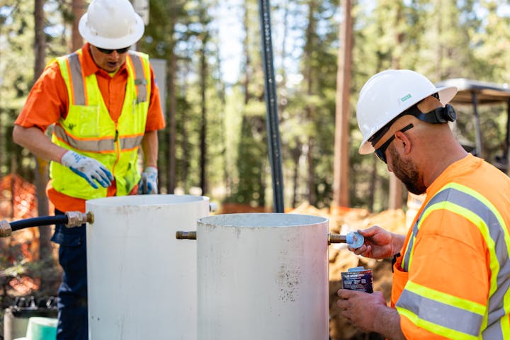 Water workers in high-visibility vests and hard hats are installing a water service at a new construction build.