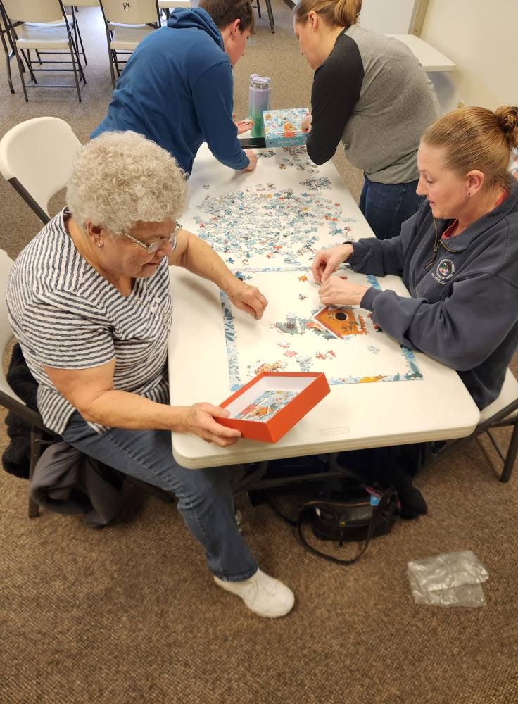 Four people gathered around a table, working on assembling a large puzzle.