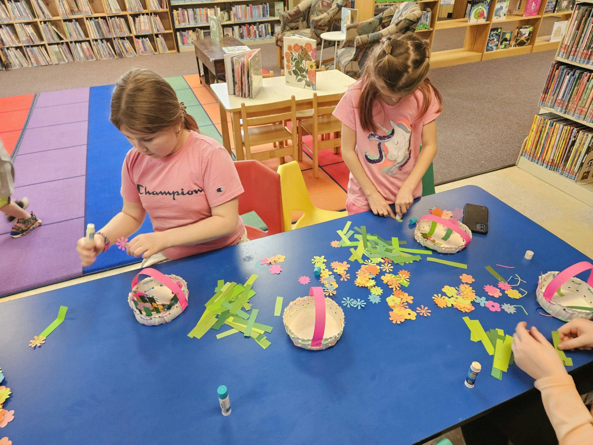 Children crafting with paper and glue at a library table.