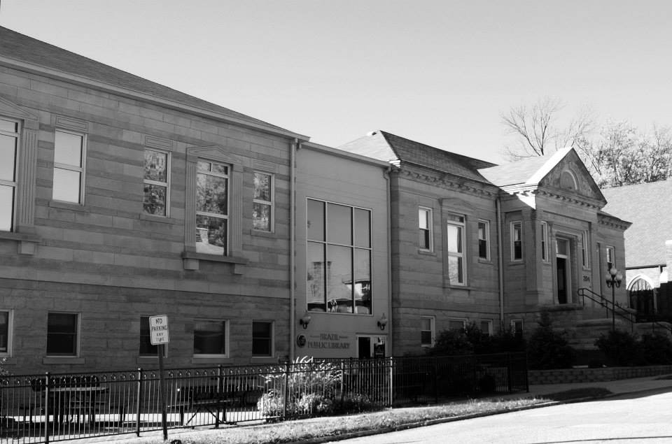 A historic library building with classic architecture, featuring large windows and a "No Parking" sign outside.