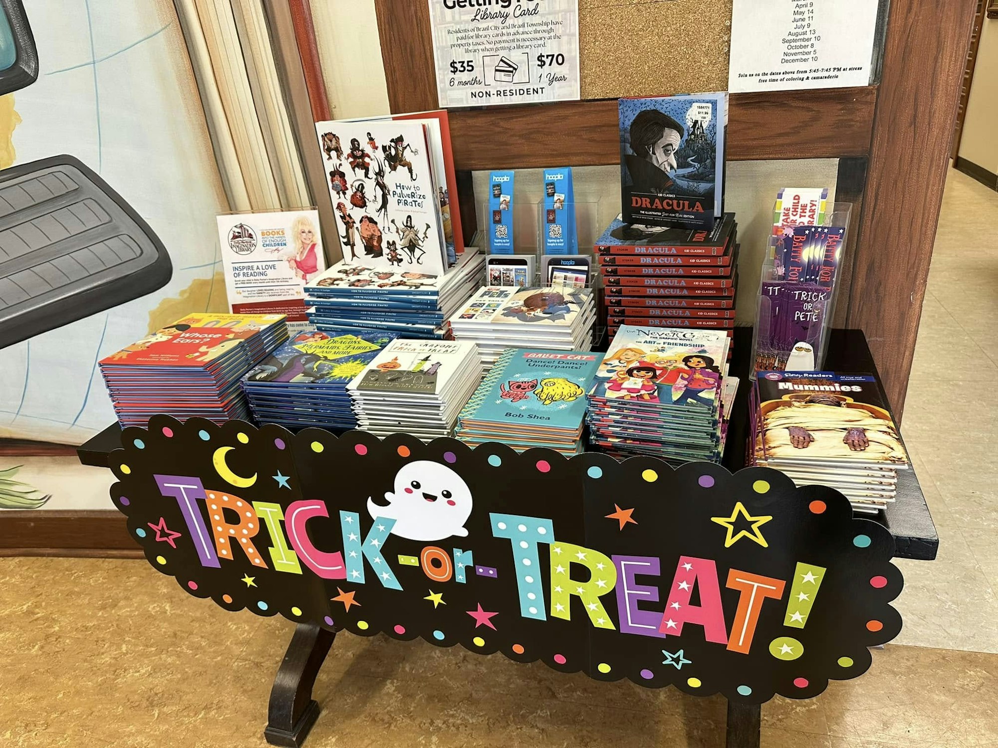 A display of children's books with a "Trick or Treat" sign featuring a ghost and Halloween decorations.