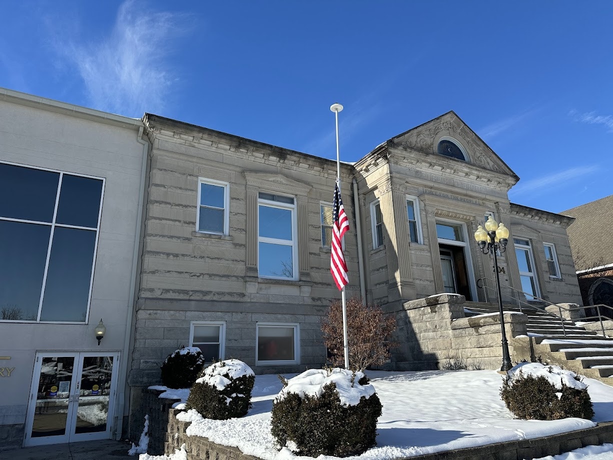 library building with clear blue sky, snow on the ground, and a flag at half mast