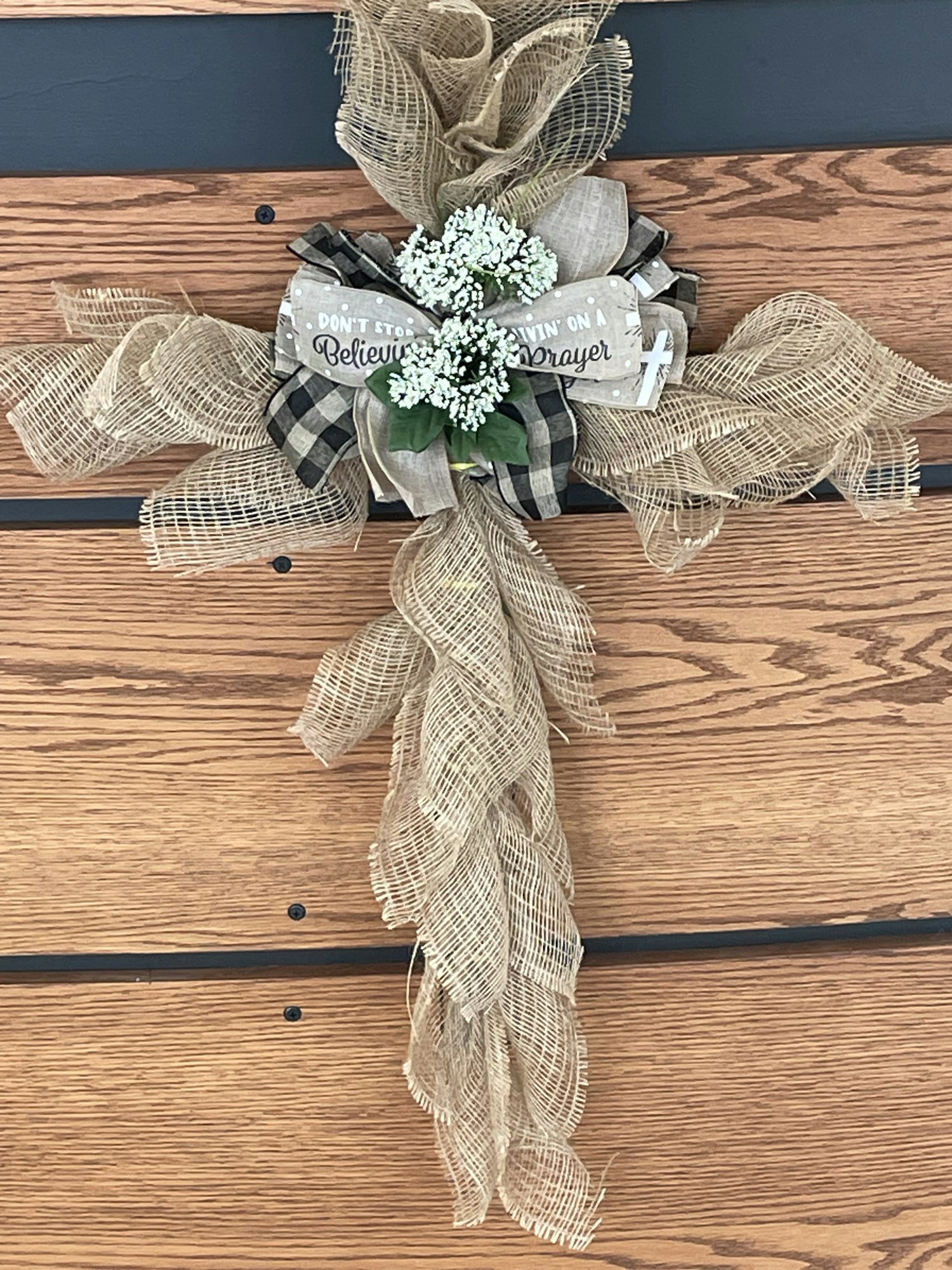 A decorative burlap cross with a ribbon, flowers, and the phrase "Don't stop believing in prayer."