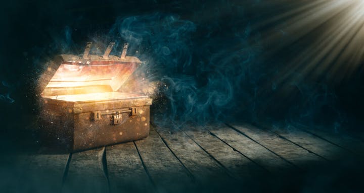An open chest emitting a bright, magical glow with beams of light and smoke on a wooden floor.