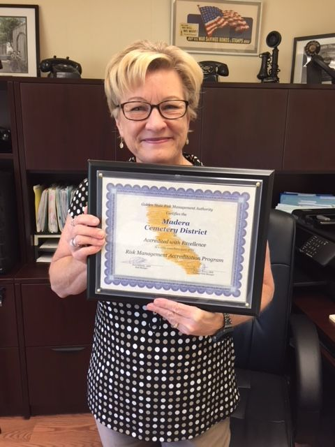 A person holding a framed certificate from Madera Cemetery District in an office setting.