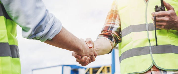 Two people in high-visibility vests shaking hands at a construction site.