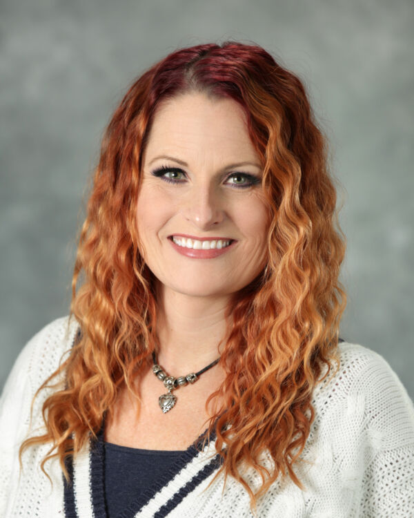 A person with wavy red hair, smiling, wearing a white sweater and a necklace.