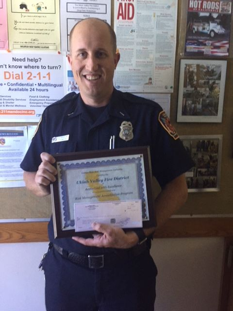 A firefighter in uniform holds an award certificate from Ukiah Valley Fire District.