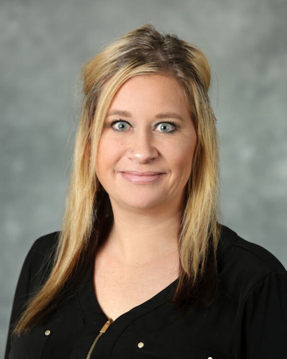 A person with long, blonde hair wearing a black top against a gray background.