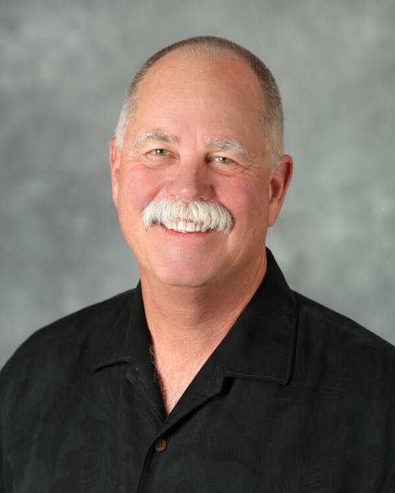 A smiling man with a mustache and a black shirt against a gray background.
