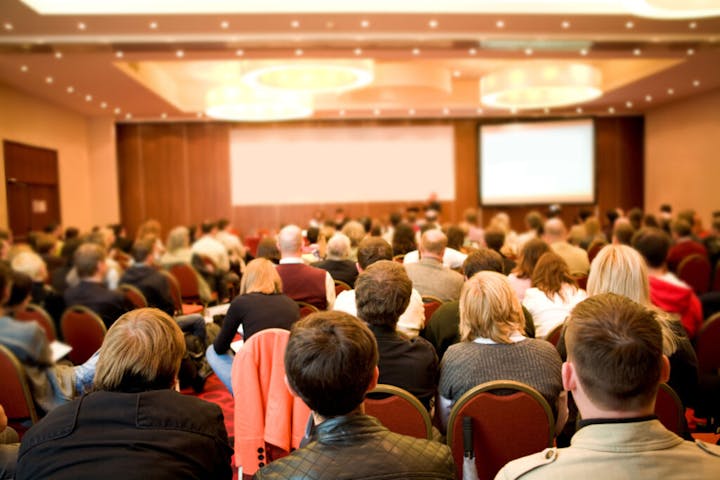 Audience sitting in a conference room facing a presentation screen.