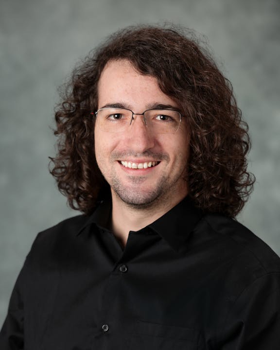 A person with curly hair, wearing glasses and a black shirt, smiling at the camera.