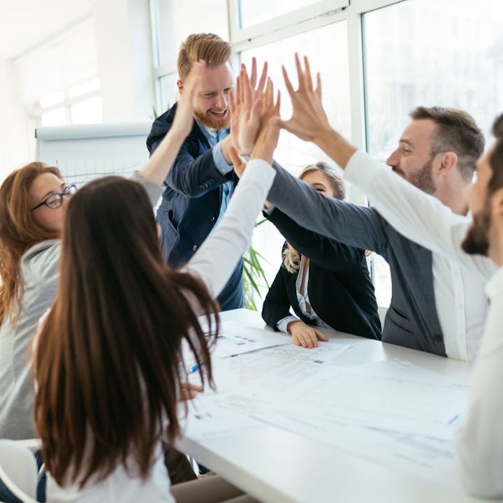 A group of people around a table giving high fives, celebrating a successful meeting or teamwork.