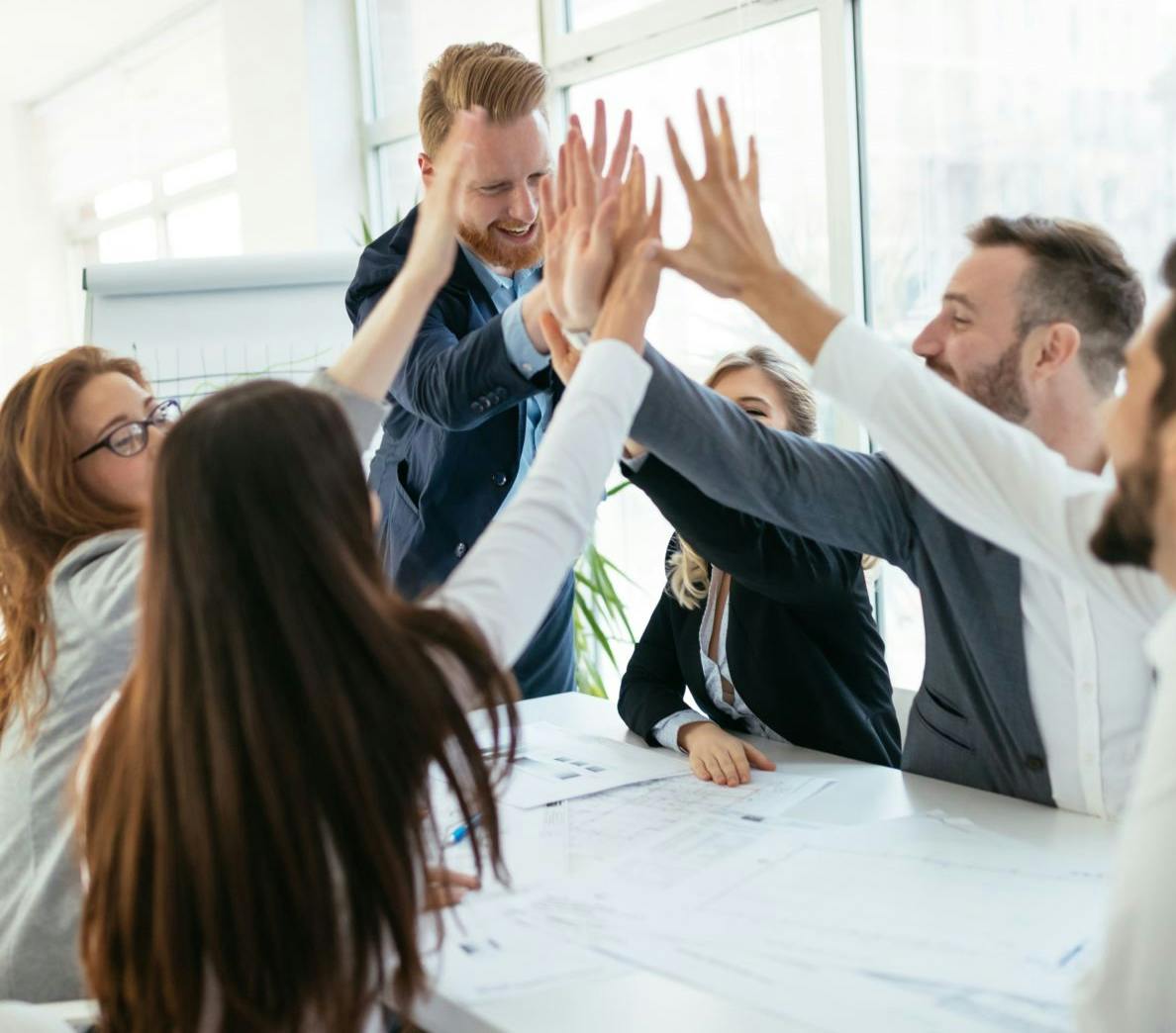 A group of people around a table giving high fives, celebrating a successful meeting or teamwork.