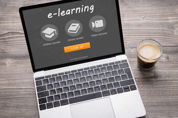 A laptop displaying an e-learning platform with options for online courses, library access, and video lectures. Cup of coffee nearby.