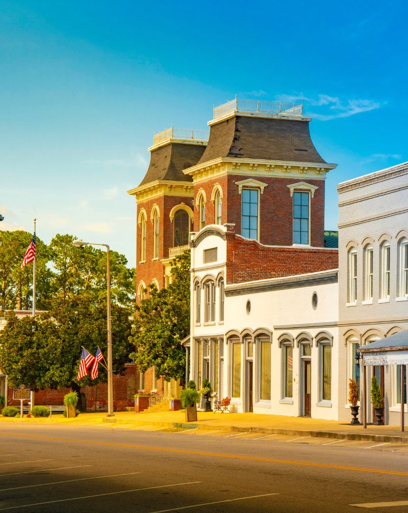 Historic brick building on a quiet street with U.S. flags, trees, and clear skies.