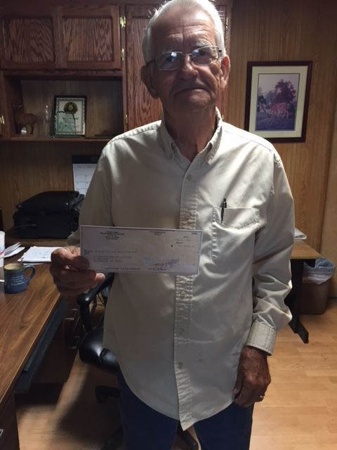 An elderly man in an office holds a check.
