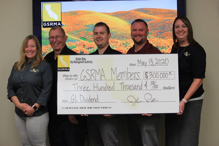 Five people holding a large check from GSRMA for $300,000 to GSRMA Members dated May 13, 2020, for GL Dividend.
