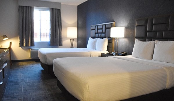 A modern hotel room featuring two beds, a large window, and contemporary decor, including lamps and dark walls.