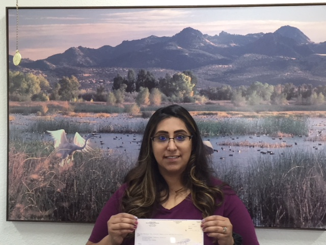 A person holding a document in front of a scenic landscape painting of mountains and a lake.