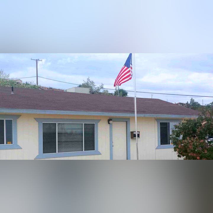 An American flag flies on a pole above a single-story house with a red roof.