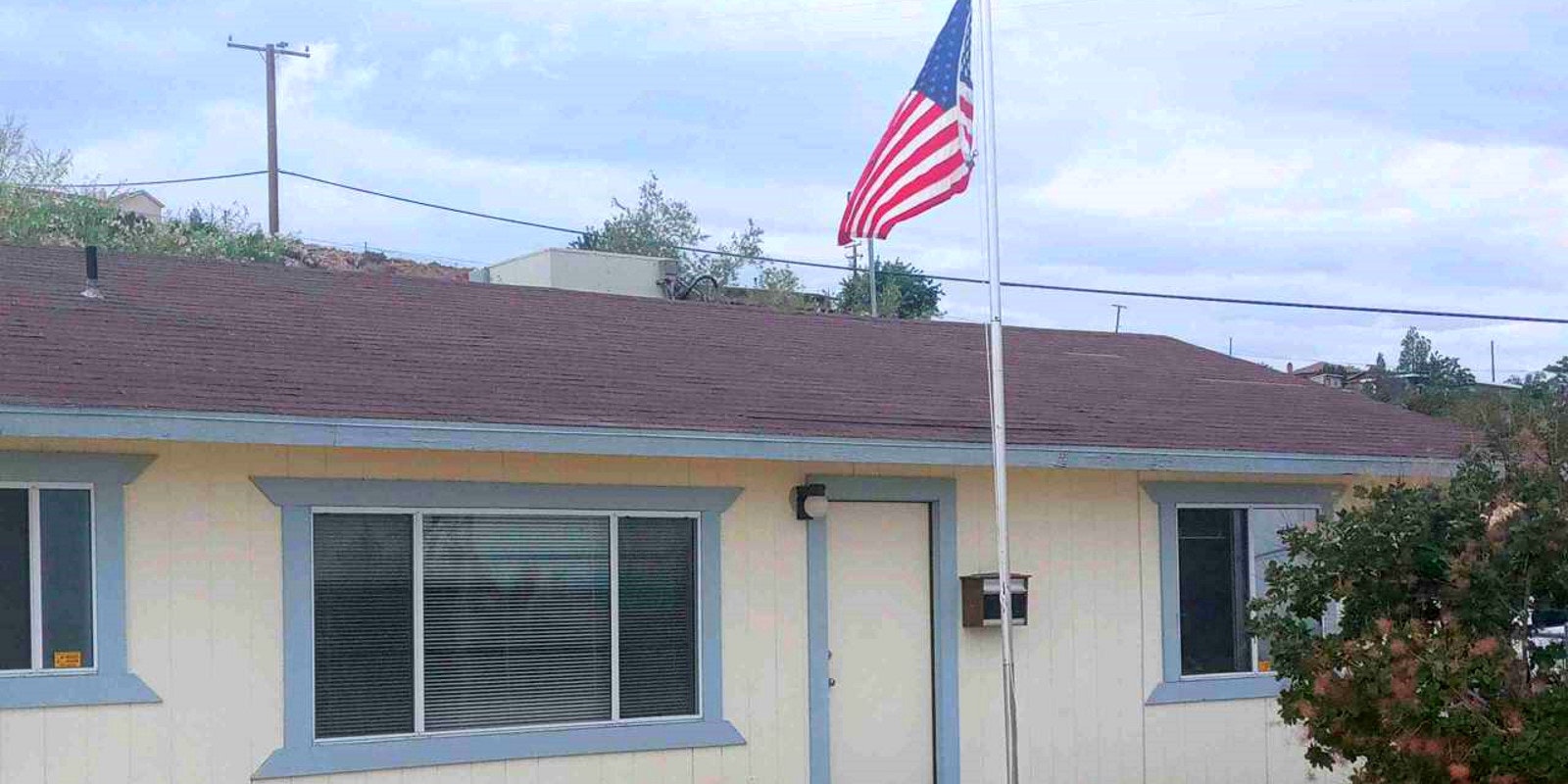 An American flag flies on a pole above a single-story house with a red roof.