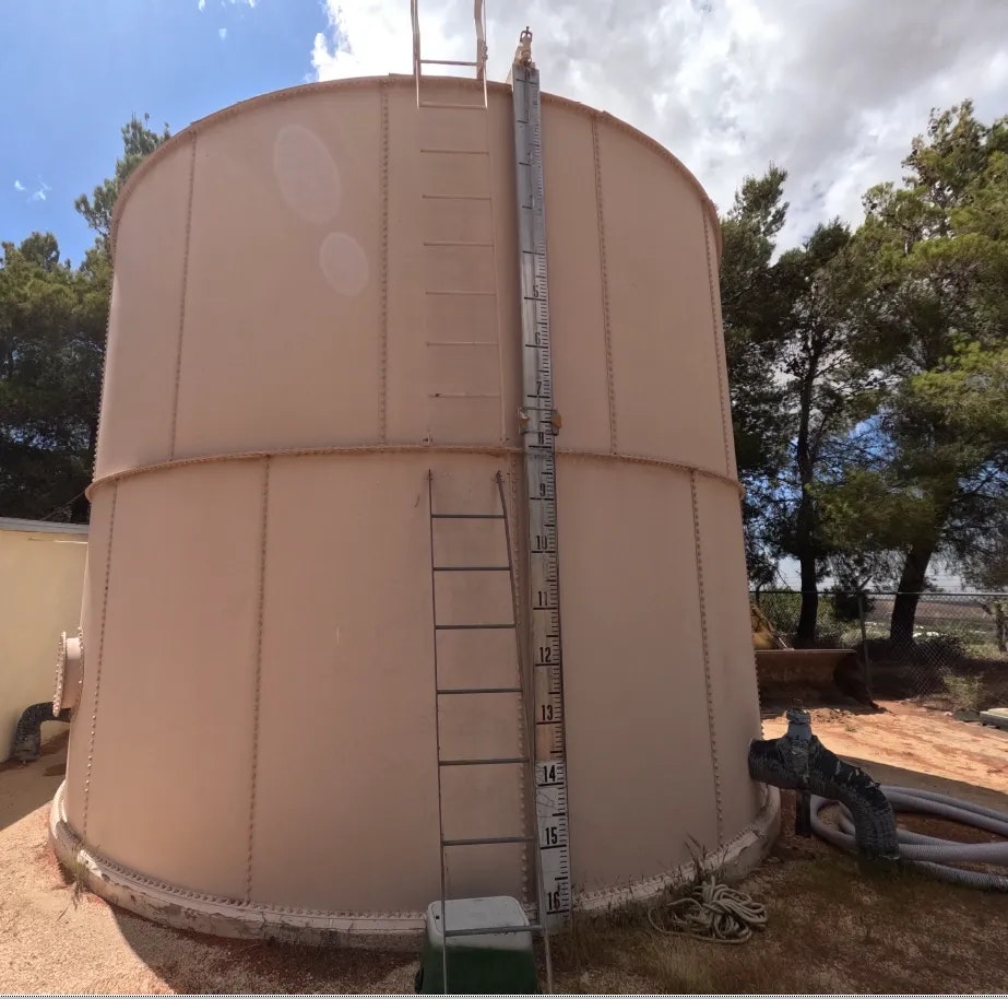 A large water storage tank with a ladder and level gauge, outdoors under a blue sky.